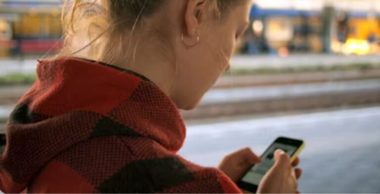 Eine Nahaufnahme einer jungen Frau, die von hinten gesehen wird, während sie ihr Handy benutzt.
