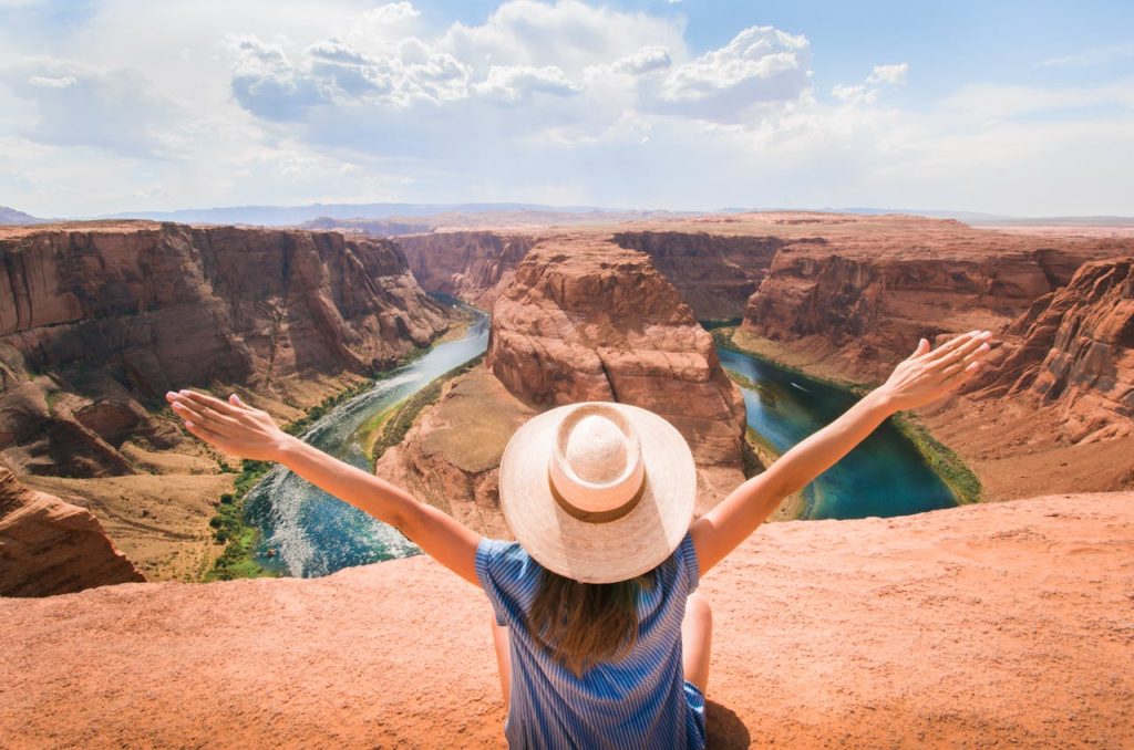 Eine junge Frau, von hinten gesehen, die vor dem Grand Canyon in Arizona die Arme hebt.