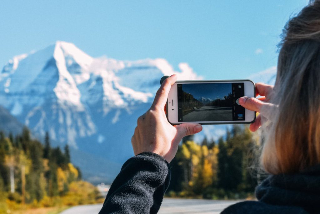 Eine Nahaufnahme einer Frau, die mit ihrem Handy Berge fotografiert.