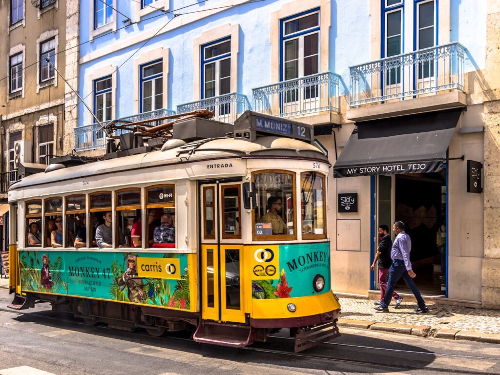 Eine bunte Straßenbahn vor der Fassade eines hellblauen Hauses in Lissabon