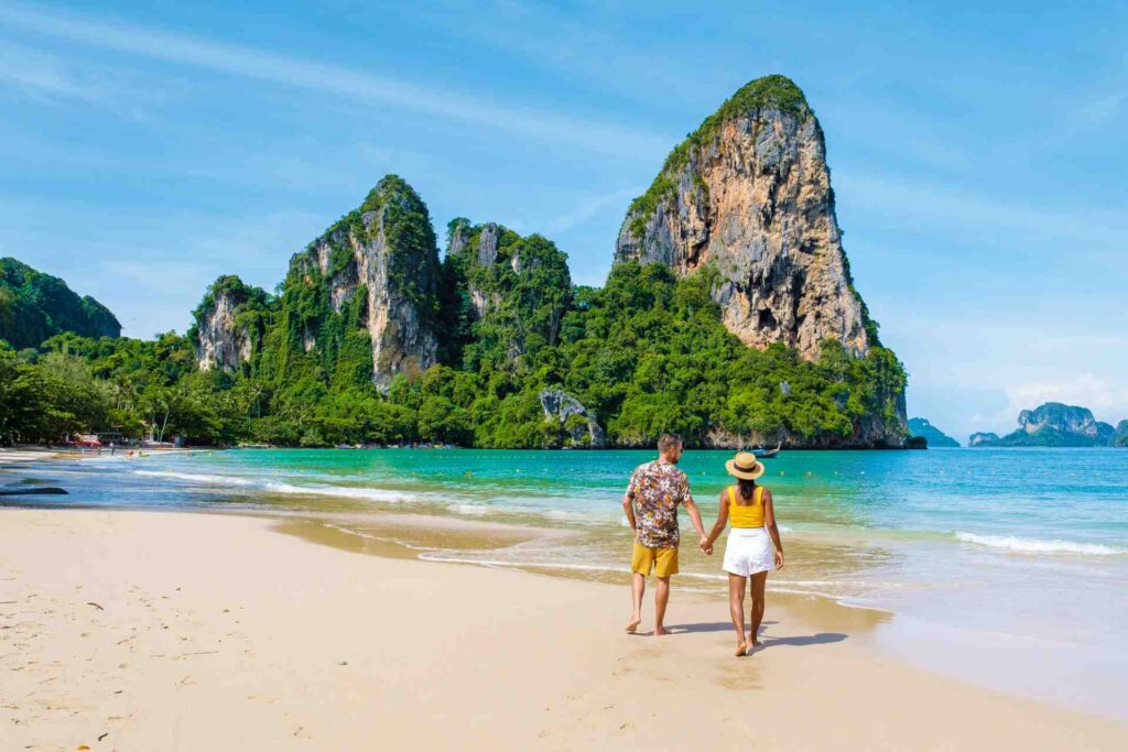 Ein Paar, das Händchen hält und am Strand von Raily in Thailand spazieren geht