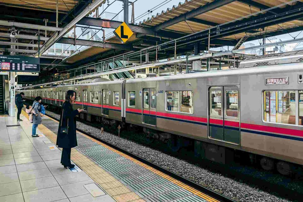 Ein stehender Zug mit wartenden Menschen auf dem Bahnsteig in Tokio, Japan.