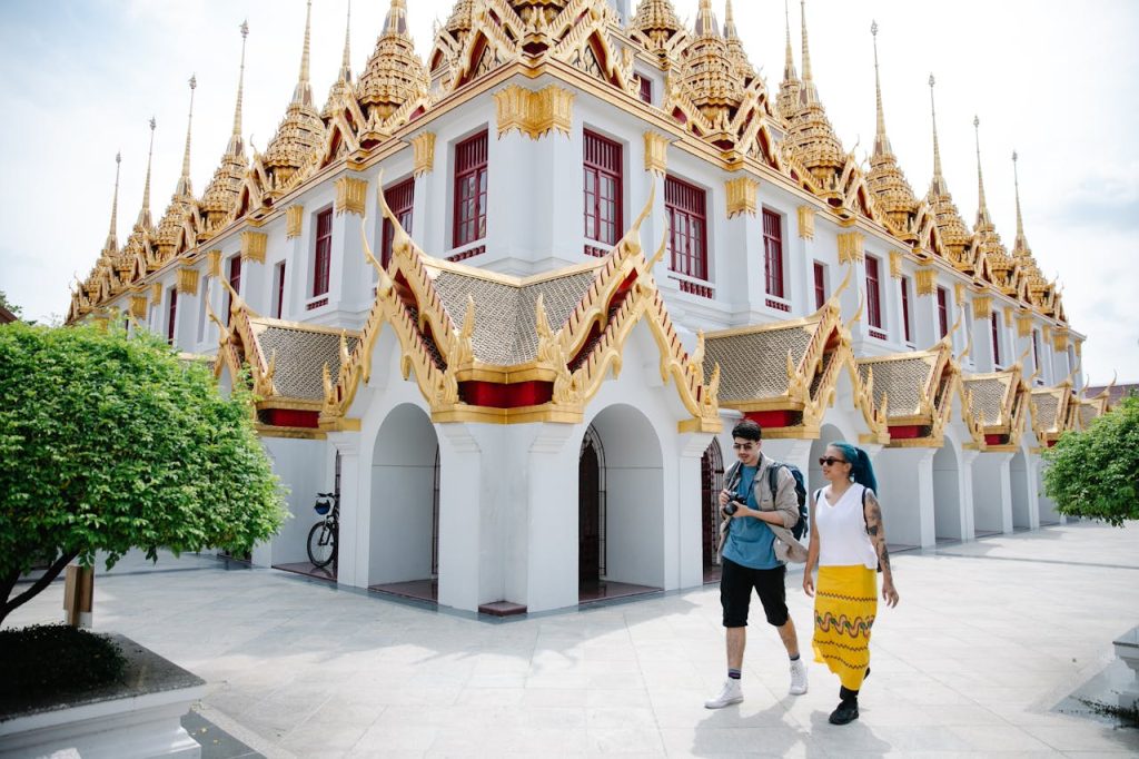 Un jeune couple de touristes devant un temple thaïlandais au toit doré.