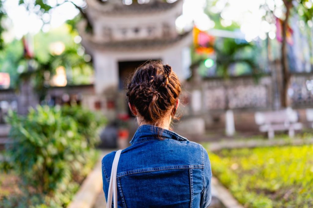 Une jeune femme vue de dos devanyt un temple au Vietnam.