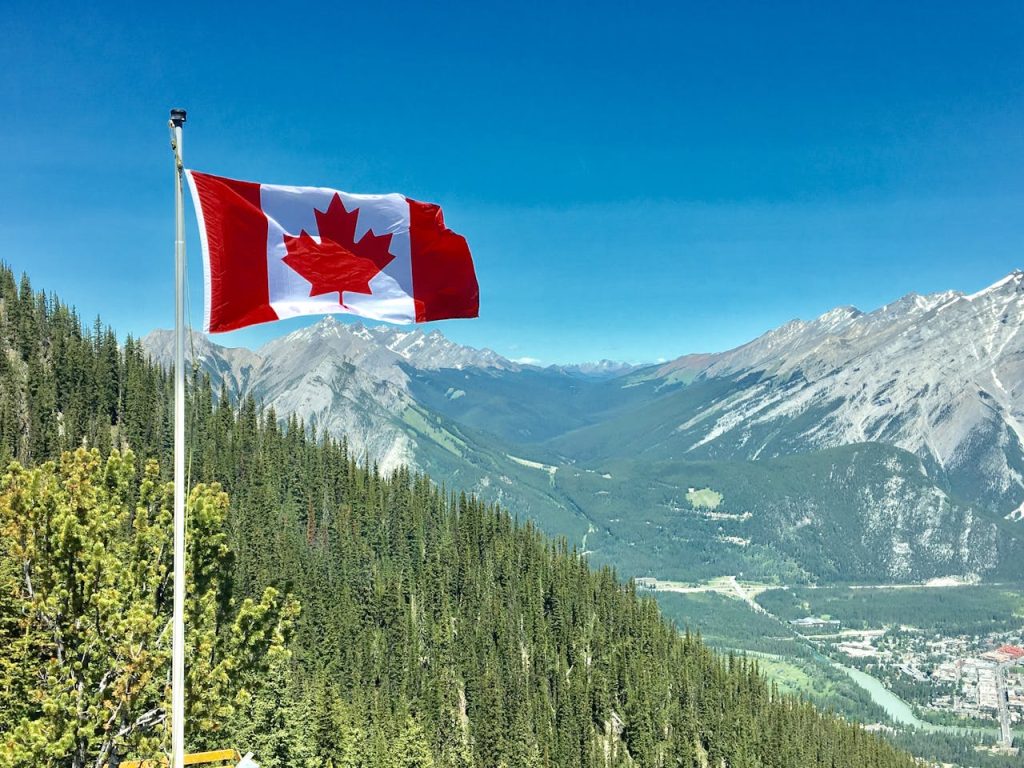 Le drapeau du Canada flottant au vent avec une chaine de montagnes en arrière-plan