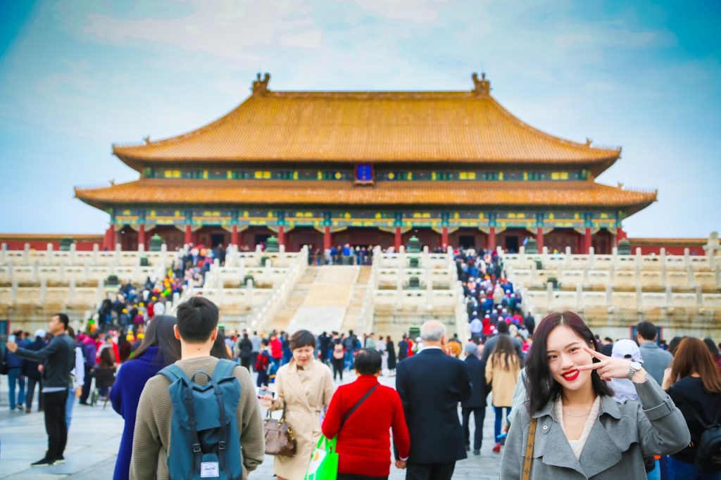 Une jeune femme souriant devant une foule de touristes venue visiter un temple en Chine.