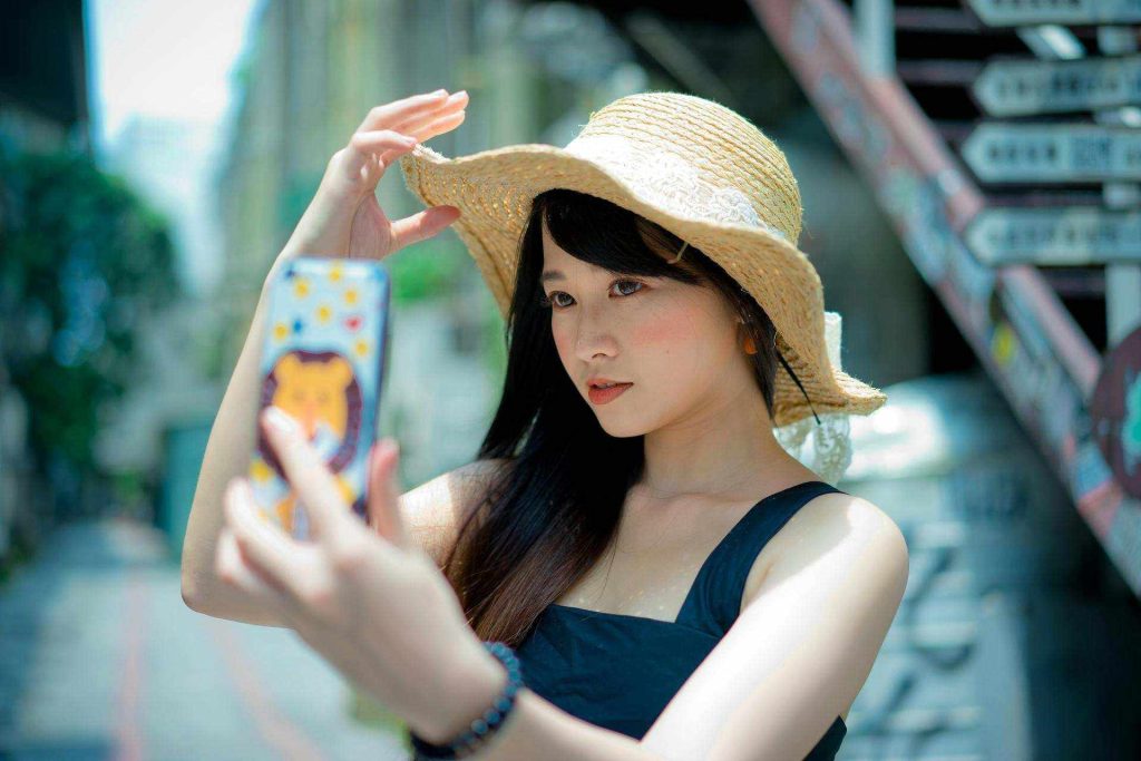 Donna che prende un selfie con un cappello estivo nel distretto Xinyi, città di Taipei, Taiwan.