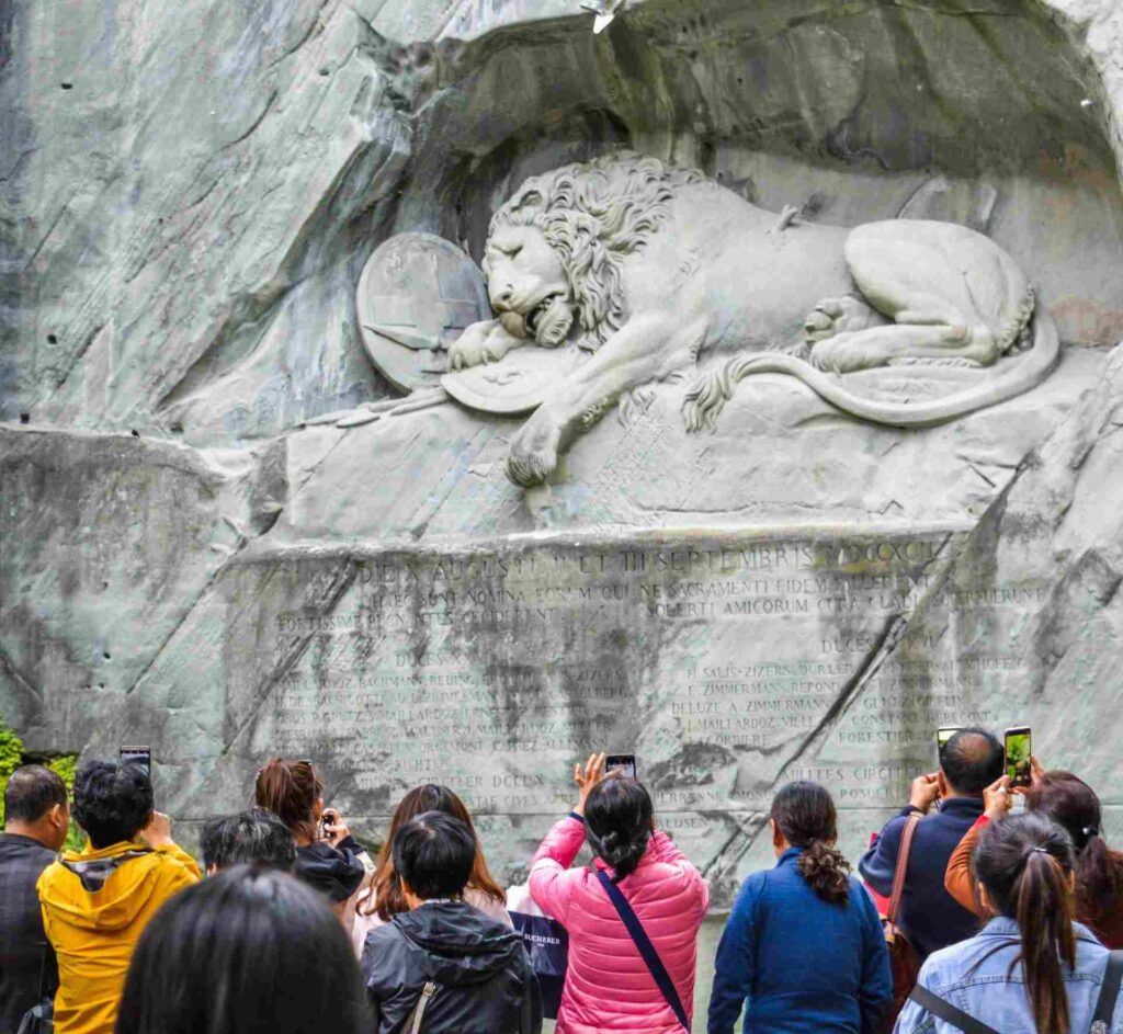 Turisti che scattano foto con il cellulare al Monumento del Leone di Lucerna.