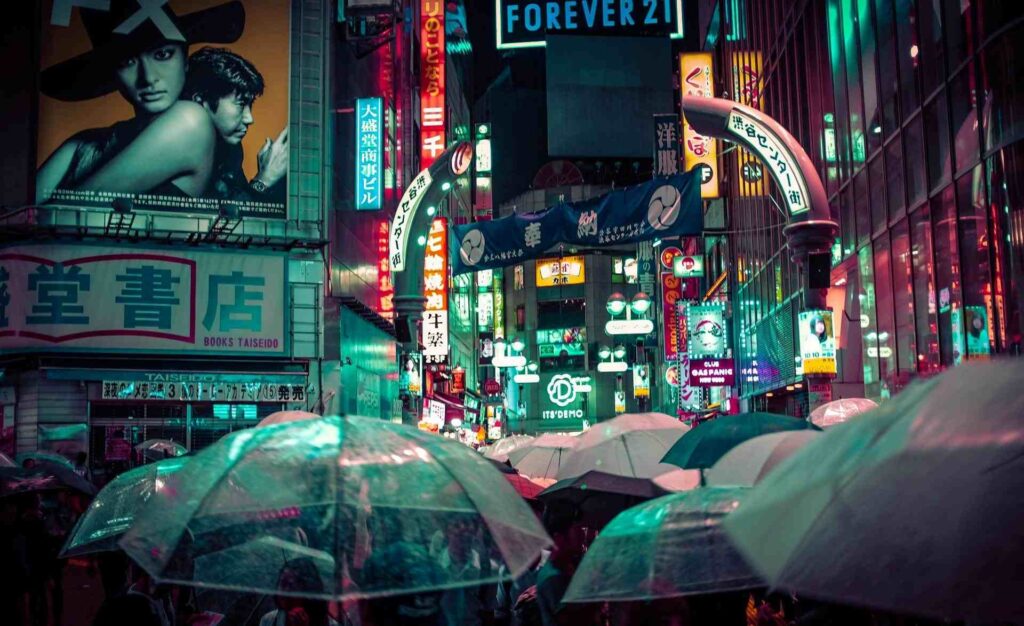 Persone con ombrelli che camminano per le strade di Tokyo di notte.