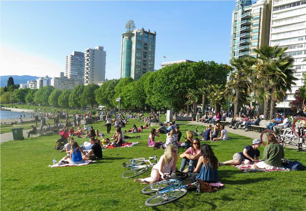 夏の日差しの下、バンクーバーのイングリッシュベイビーチで芝生に座ってリラックスする人々の光景。