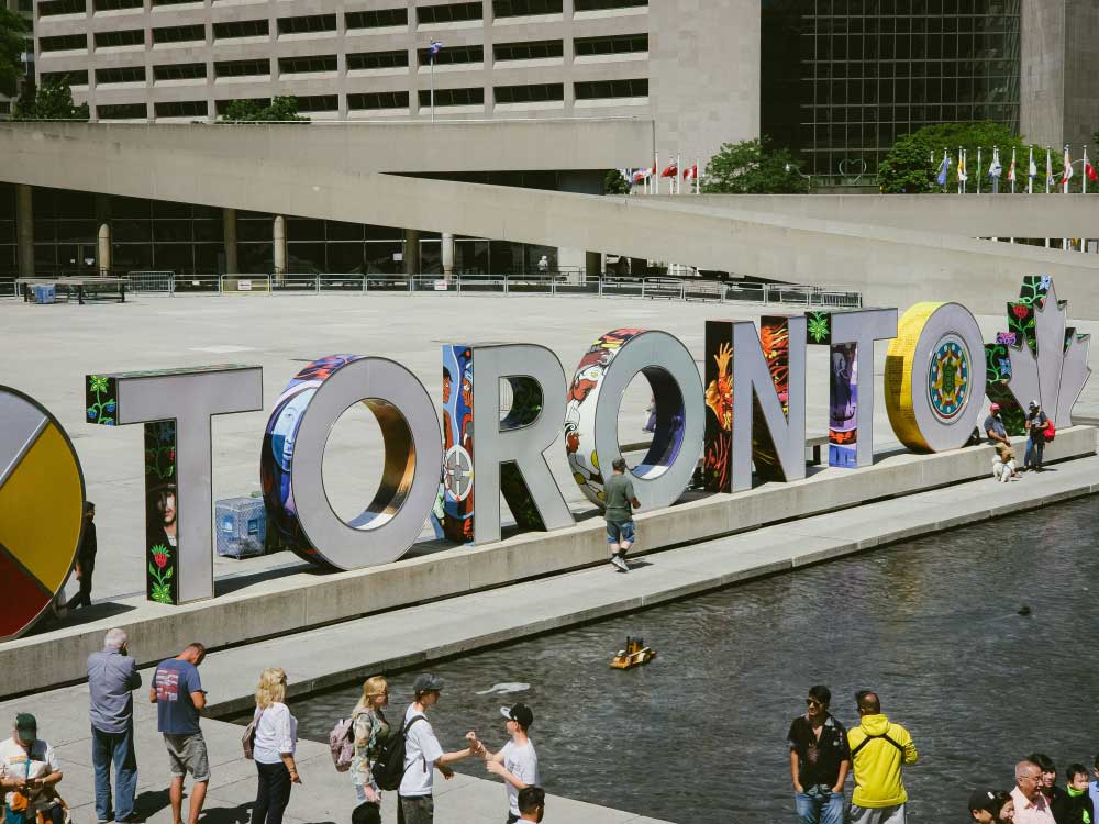 トロントのネイサンフィリップススクエアに設置されたカラフルなTORONTOサインと、その前で観光客が写真を撮る光景。