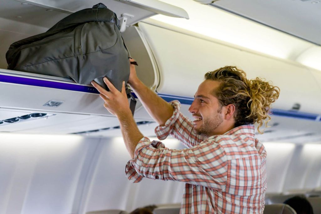 man putting his carry on into the overhead compartment