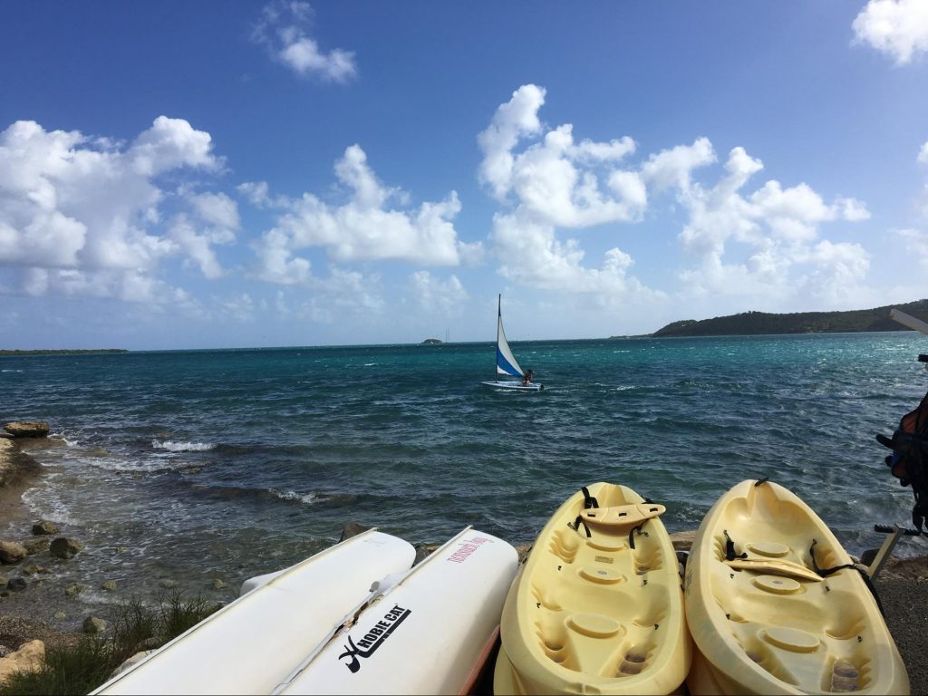 Kayaks and a sailboat by the water with a beautiful sky of clouds in the Caribbean